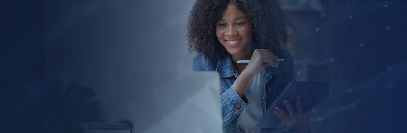 A smiling woman with curly hair sits at a desk, looking at her laptop while holding a pen and tablet. She appears focused and engaged in online learning, set against a dark blue background with subtle network-style graphic lines.