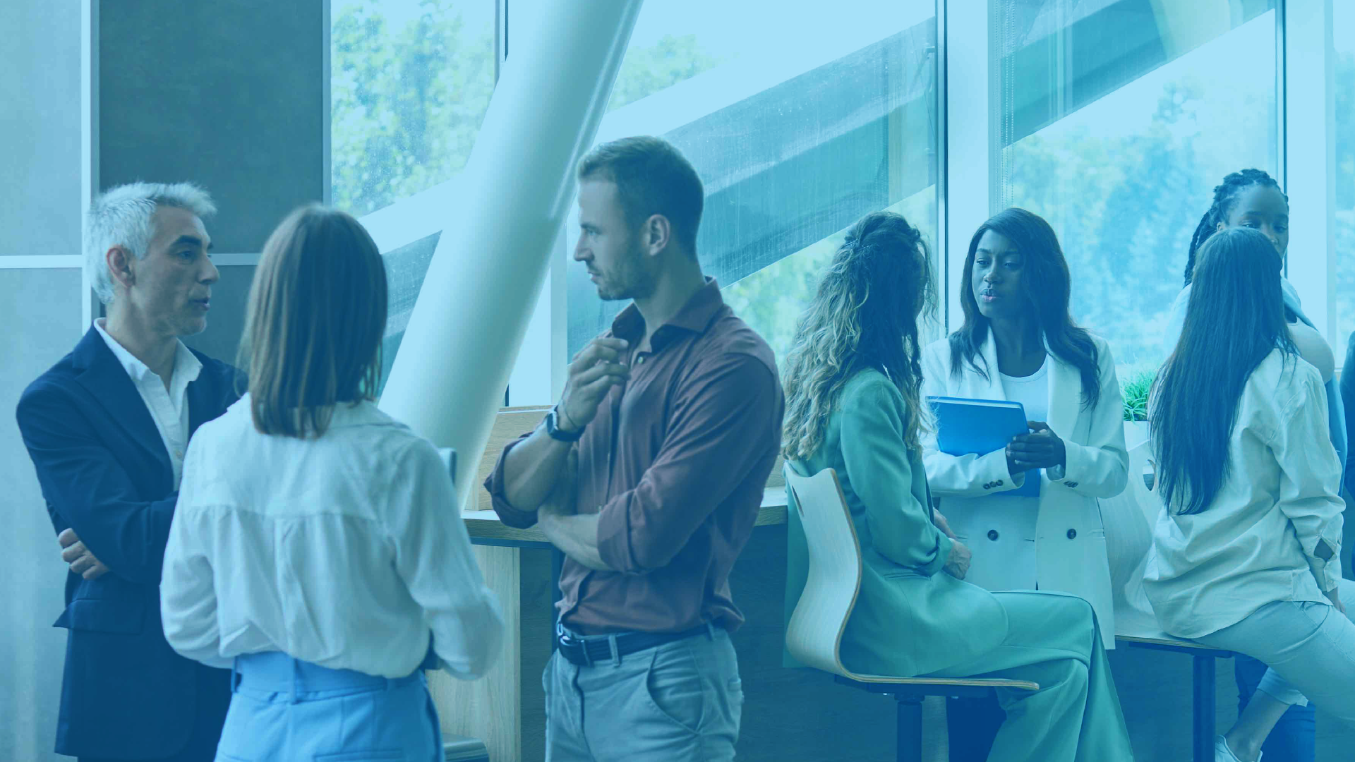 A diverse group of professionals networking and talking in small groups inside a modern, light-filled conference or office space.