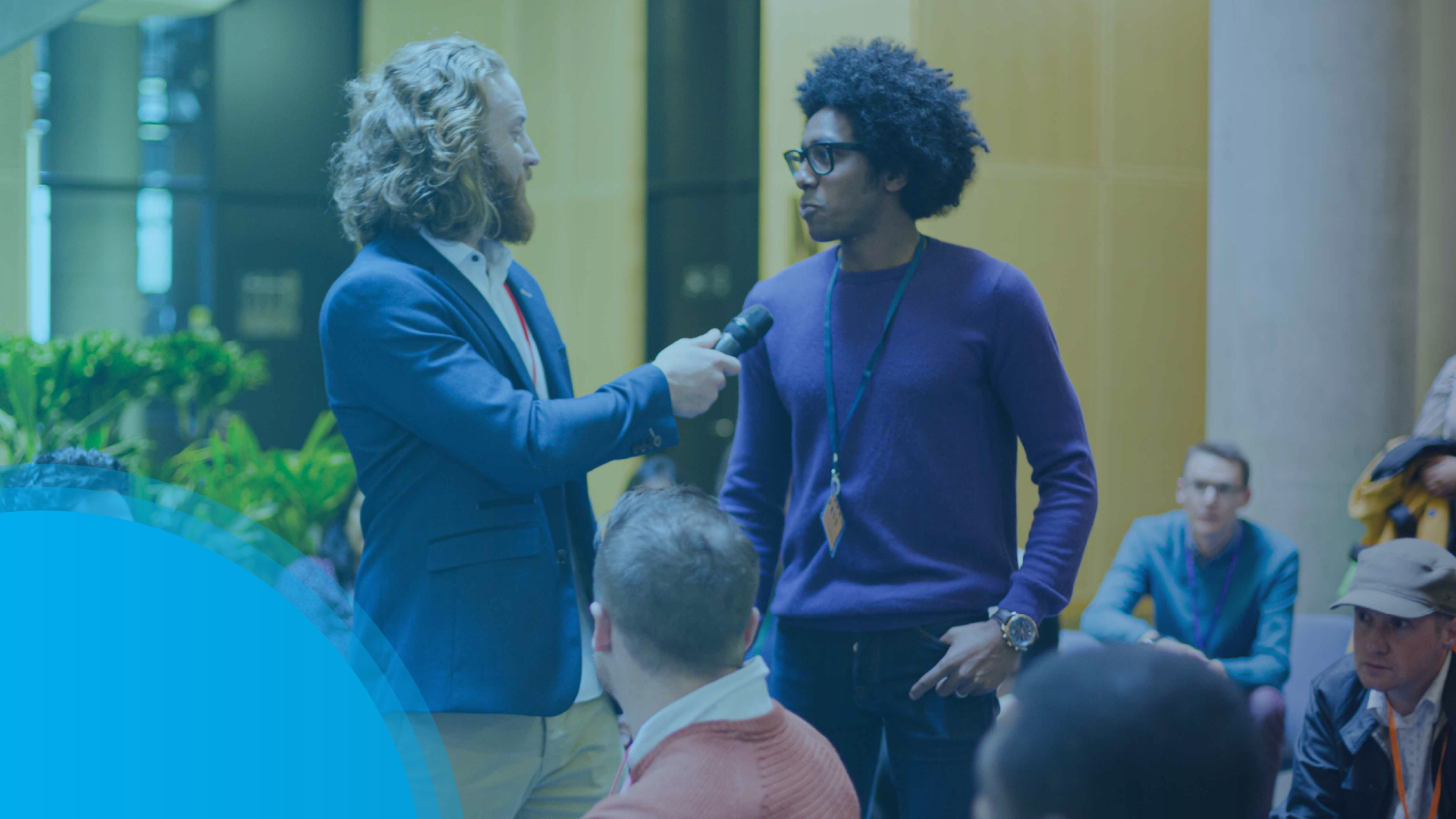 Person holds a microphone toward a speaker wearing a lanyard during a group discussion.