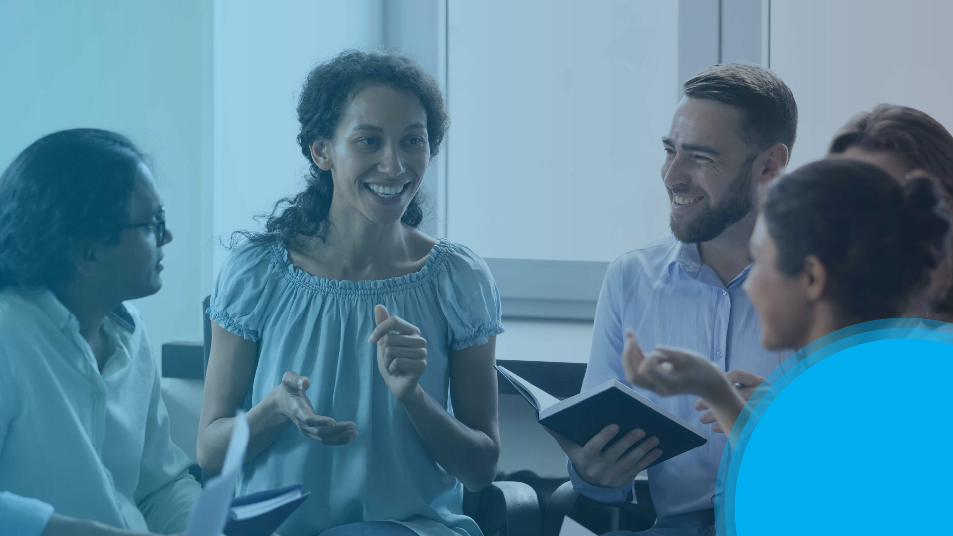 Small group in a meeting smiles and talks while holding notebooks.