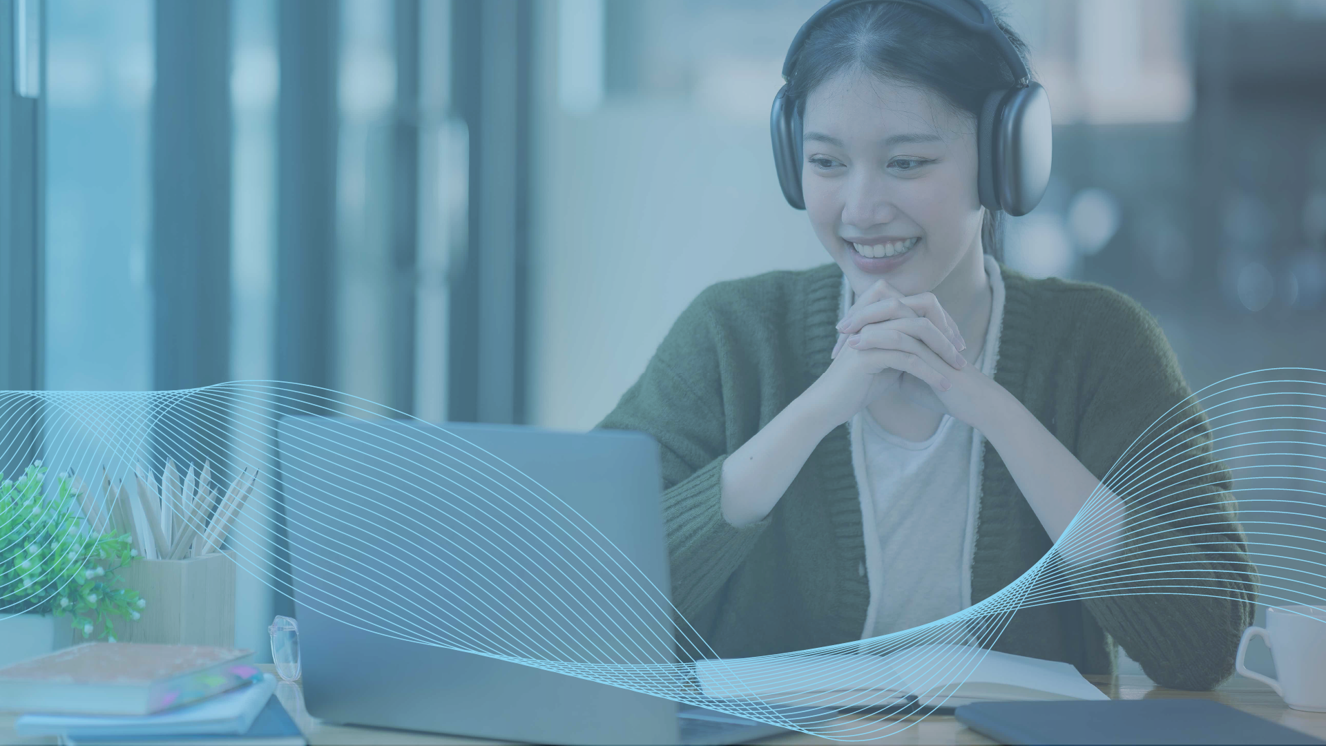 Smiling person wearing headphones looks at a laptop during an online session at a desk.